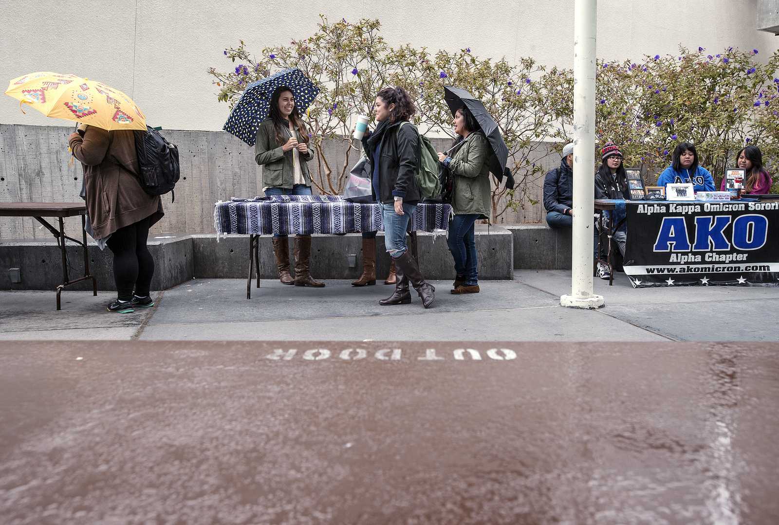 As rain falls down on Malcolm X Plaza, Devoted Women for Change is the last of the organizations to remain tabling. Members Selena Galvez, Karina Rojas, leiloni lund and Alexis Godinez (middle table, left to right) are in the club because they want to set up a Sigma Lambda Gamma chapter at SF State. Photo by Benjamin Kamps / Xpress