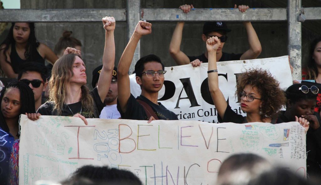 Seanan Kenney, Jon Ray Guevarra, and a fellow student raise their fists and hold a banner saying I believe in ethnic studies to show their support for the College of Ethnic Studies in Malcolm X Plaza at SF State, Thursday, Feb. 25, 2016. (Mira Laing / Special to Xpress)