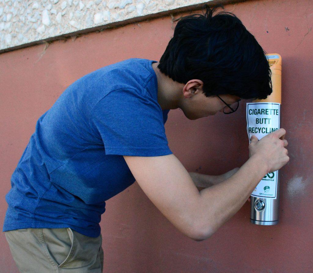 SF State student An Bui places the identifying sticker on the cigarette recycling bin located along Tapia Dive, Thursday, March 17, 2016. (Connor Hunt / Xpress)