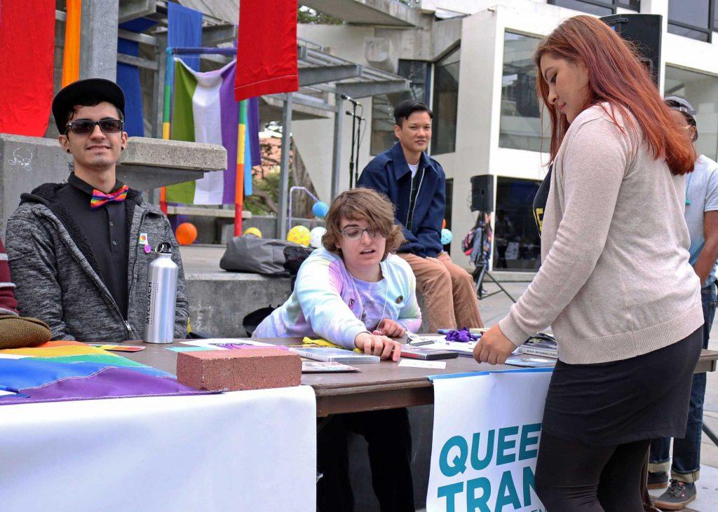 Queer Alliance and Trans Center members Alan Martinez (left) and Lauren Wolf (center) speak to a SF State student during the Coming Out Day event in Malcolm X Plaza on Monday, Oct. 10, 2016.