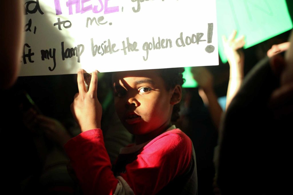 Rode Hartsough, an 8-year-old San Francisco resident, carries a picket sign with the Statue of Liberty poem written on it at the arriving terminals of the SFO International Airport in San Francisco, Calif. on Saturday, January 28, 2017. (Janett Perez)