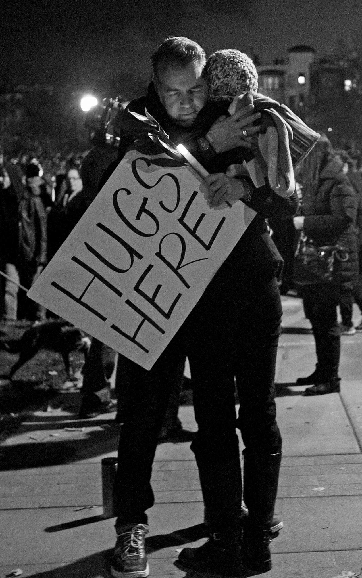 A person holding a Hugs Here sign hugs another person during a candlelight vigil for the victims of the Ghost Ship artist warehouse fire, at Lake Merritt in Oakland, Calif. on Monday, Dec. 5, 2016 (George Morin/ Xpress).