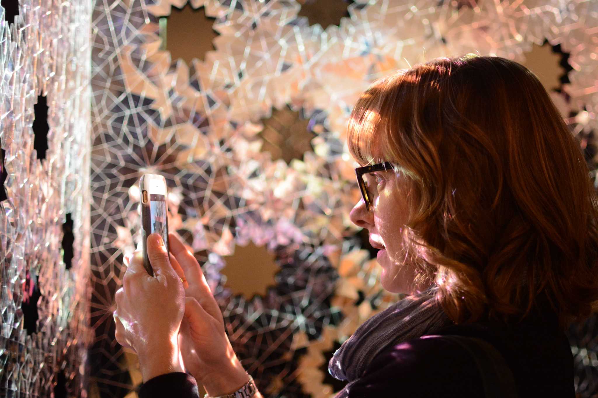 Michelle Jones, 39, an art history major at SF State from San Carlos, Calif. uses her phone to photograph Sanaz Mazinanis reflective, visual and sound-based art piece Threshold during the Mashrabiya - the art of looking back - art gallery opening reception in the Fine Arts building at SF State on Saturday, February 18, 2017. (Aaron Levy-Wolins / Xpress)