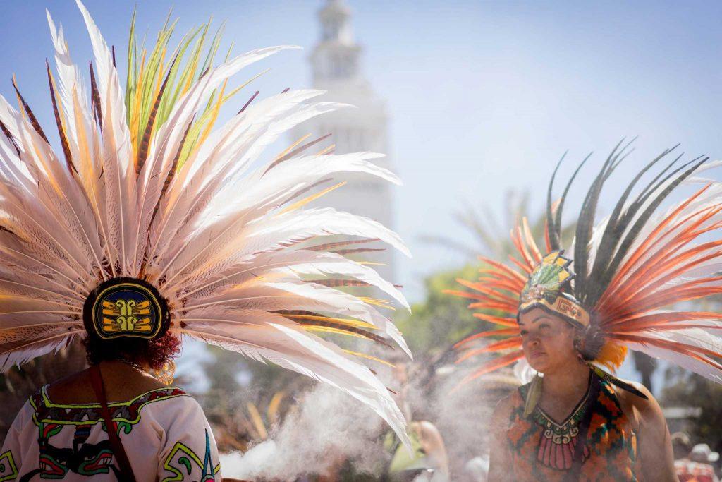Maya Ponce (right) speaks with a fellow traditional Aztec dancer from the Xiuhcoatl group at the May Day protest down Embarcadero Street on Monday, May 1, 2017. (Sarahbeth Maney/Xpress).