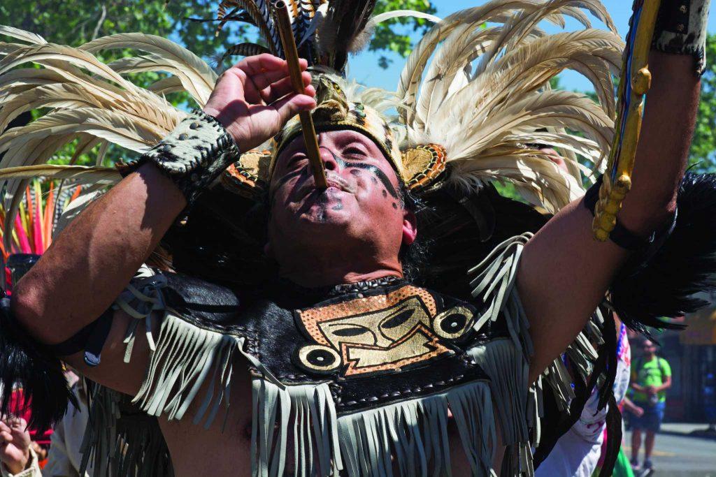 Alvaro Tellez plays music with a carrizo, an Aztec flute, while performing Aztec traditional dance to bless the May Day March in Oakland, Calif. on Monday, May 1, 2017. (Lee Kin/Xpress)