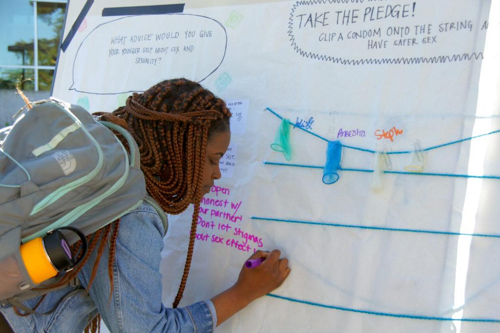 A health education major student Dede Creppy writes a message on the board during National Condom Month launch event at SF State on Wednesday, Feb. 7, 2018. (Aya Yoshida/Golden Gate Xpress)