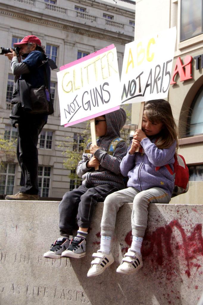 Jacob Brunner, left, and Chloe Brunner, right, with signs sit and watch people marching towards Embarcadero in San Francisco on Saturday, March 24, 2018. (Aya Yoshida / Golden Gate Xpress)