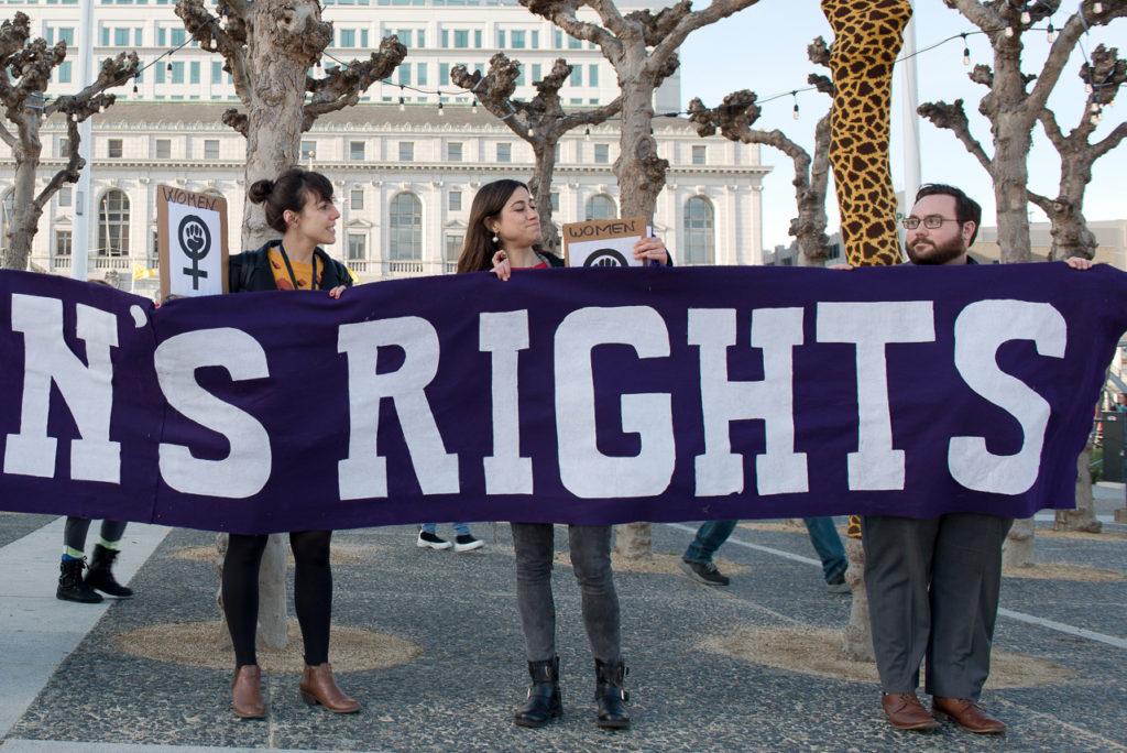 Carolina Alquezar, left, and Olatz Arteaga, center, protest against womens inequality around the world by holding a banner that read as womens rights in front of San Francisco City Hall on March. 08, 2018. Both are Spain natives who came to celebrate International Womens Day in San Francisco. (David Rodriguez/Golden Gate Xpress)