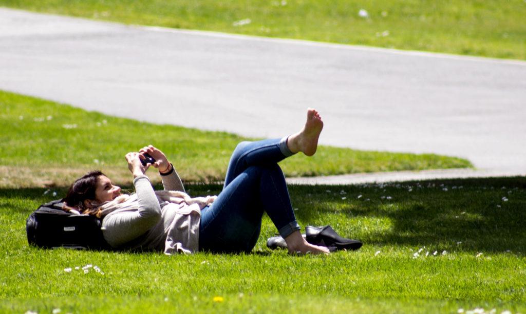 A+SFSU+student+uses+their+phone+on+a+sunny+day+while+laying+on+the+grass.+Photo+by+Jordi+Molina