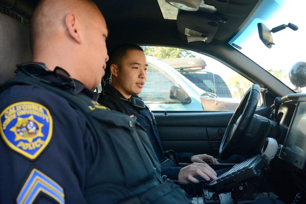 Cpl. Enrique Vera Cruz (left) chats with Officer David Lin (right) in a squad car by the University Police Department station at SF State in San Francisco, Calif., on Thursday, Dec. 6, 2018. Vera Cruz, a six-year veteran of the SF States police force, is training Lin - who recently graduated from a police academy. (Aaron Levy-Wolins)