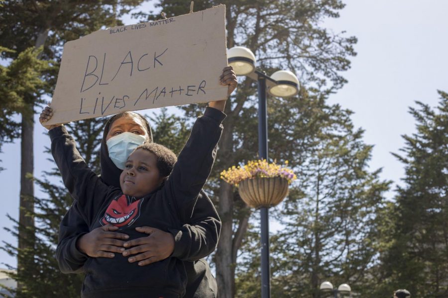 Jace Smith holds up a sign that says, “BLACK LIVES MATTER,” while his mother, Veronica Smith, holds him during a peaceful protest against police brutality and systemic racism in front of SF State at 19th and Holloway on Sunday, June 7, 2020. (Emily Curiel / Golden Gate Xpress)