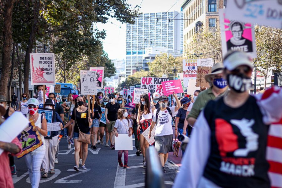 People march down the Market Street holding various signs related to womens rights, honoring the late Justice Ruth Bader Ginsberg, voting President Trump out, and urging people to go out and vote, during Womens March in San Francisco on Oct. 17, 2020. (Harika Maddala / Golden Gate Xpress)