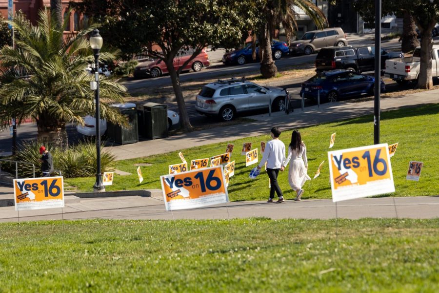 People walk by Proposition 16 signs  staked in the grass towards the entrance of Mission Dolores Park on Oct. 31. Proposition 16 would restore affirmative action at public institutions in the state of California. (Jun Ueda / Golden Gate Xpress)