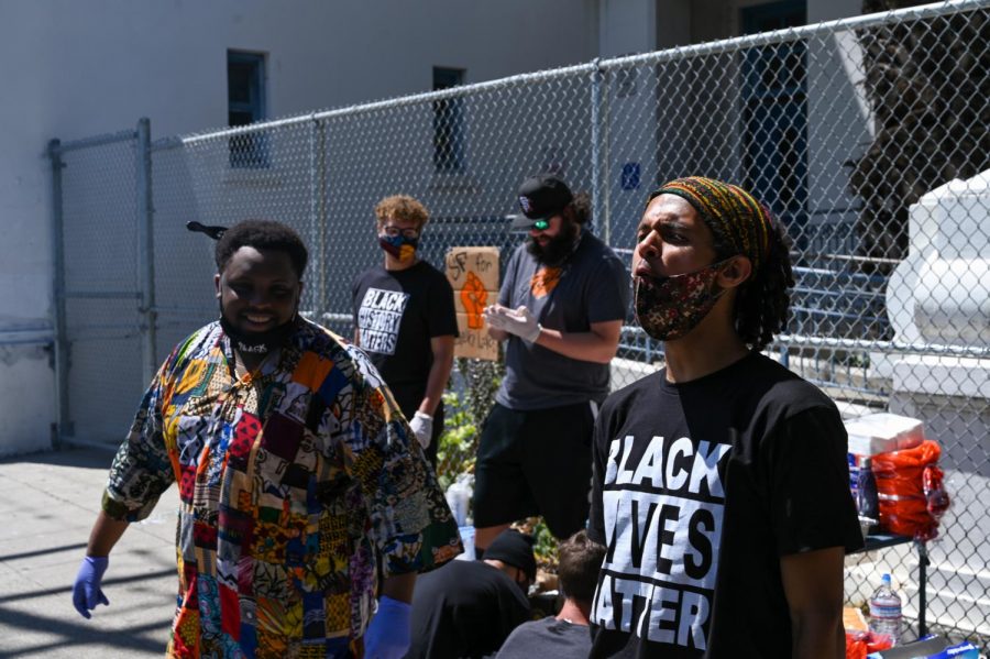 Organizers of a bbq promoting positive community relationships laugh while promoting the event through signs during a Juneteenth celebration organized in San Francisco, on June 19, 2020. (James Wyatt / Golden Gate Xpress)