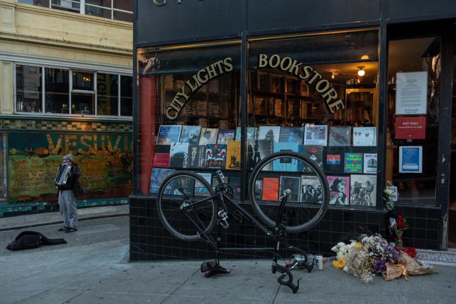 A man plays an accordion next to City Lights Books on Tuesday, February 23, 2021 in San Francisco. Flowers and candles are left in front to honor the Lawrence Ferlinghetti, who died on Monday evening at the age of 101. (Cameron Lee / Golden Gate Xpress)