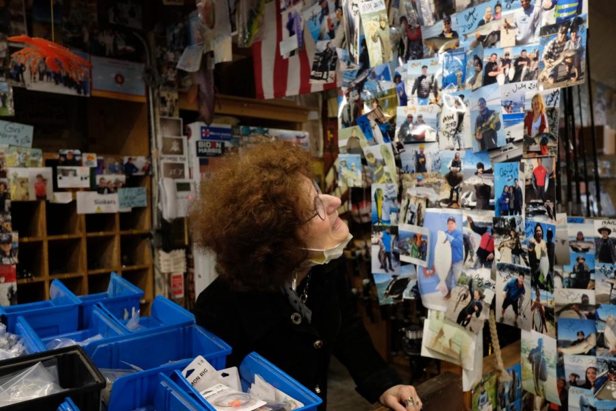 Stephanie Ernst Scott recounts one of the hundreds of stories behind the photos that line the entryway into Gus’ Discount Tackle. Customers and friends have built up the shrine-like collection over decades. (Avery Wilcox / Golden Gate Xpress)