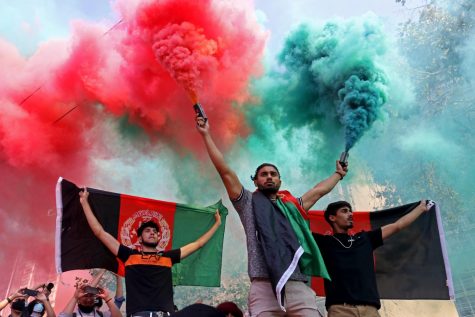 A demonstrator diffuses two colored smoke grenades, which represent the Afghanistan flag, and two participants hold the flag to the crowd on Market Street during a peaceful protest on Aug. 28, 2021. 