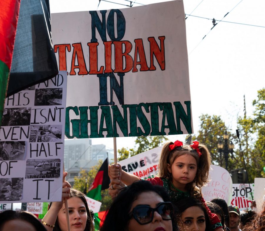 A young girl holds up a sign stating “No Taliban in Afghanistan” while on her mother’s shoulders as they walk down with the crowd on Market Street on Aug. 28, 2021. (Samantha Laurey / Golden Gate Xpress)