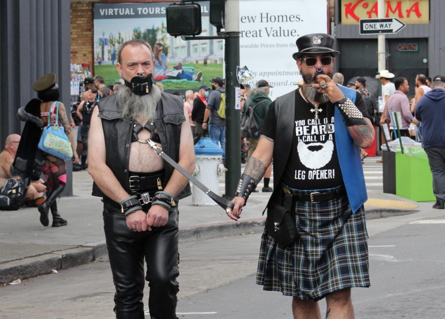 John smokes a cigar while Jason follows him on a leash at Folsom Street Fair on Sept. 26, 2021. Folsom Street Fair returns from its COVID hiatus with the theme ‘Megahood 2021,’ an in-person event named after the first fair held in 1984. The fair provided resources for COVID-19, HIV and other healthcare needs throughout the day. (Paris Galarza/Golden Gate Xpress)