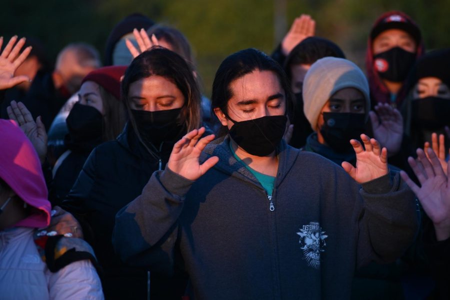 A man raises his hands with others in prayer as the sun rises on Alcatraz Island on Oct. 11, 2021. The prayer was motivated to help bring in healing attributes to those within the gathering, as they spent the early morning reflecting on Indigenous history. (Samantha Laurey / Golden Gate Xpress)