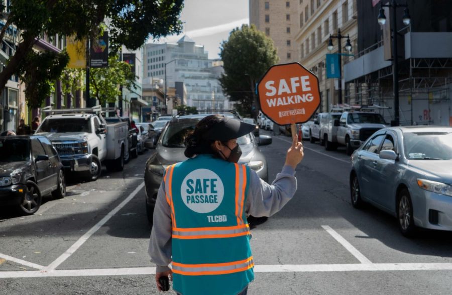 Maria Cortez, a corner captain for Safe Passage, holds up a sign that says ‘Safe Walking’ to stop incoming traffic to give pedestrians more time to cross the street on Monday. (Rashik Adhikari / Golden Gate Xpress)