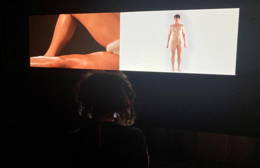 An attendee sits down to watch one of the video displays at the Fine Arts Gallery during the “Beyond Binary” opening ceremony on Sept. 17. The piece, titled “Fast Twitch // Slow Twitch,” was made by the artist Cassils in 2011. (Aiden Brady / Golden Gate Xpress)