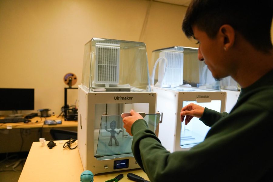 Engineering student Gerardo Nunez opens the cover to a 3D printer in Thornton Hall on Sept. 12, 2022. Inside sits a plastic replica of Baby Groot from the blockbuster film, “Guardians of the Galaxy.” “We get to make all kinds of stuff in here,” Nunez said. (Joshua Carter / Golden Gate Xpress)