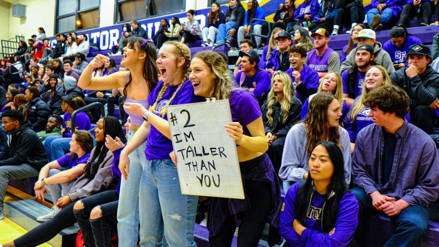 SF State student Trinity Yates holds up a whiteboard making fun of an opposing player’s height while watching the SFSU vs CSU San Bernardino basketball game with other students in the Main Gym at Don Nasser Plaza on Dec. 1, 2022. (Miguel Francesco Carrion / Golden Gate Xpress) 