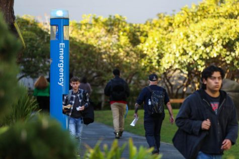 Students walk past a blue emergency phone pole in SF States Garden of Remembrance on Dec. 7, 2022. These emergency phones, which are placed around campus call campus police when the button is pushed. (Juliana Yamada / Golden Gate Xpress)