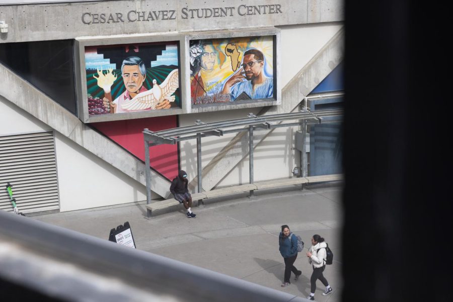 An individual sits beneath the Malcolm X mural on the facade of the Cesar Chavez Student Center building at SF State on Thursday, Feb. 16, 2023. The 27th annual celebration of the mural is planned to be held on Tuesday, Feb. 21. (Benjamin Fanjoy / Golden Gate Xpress)