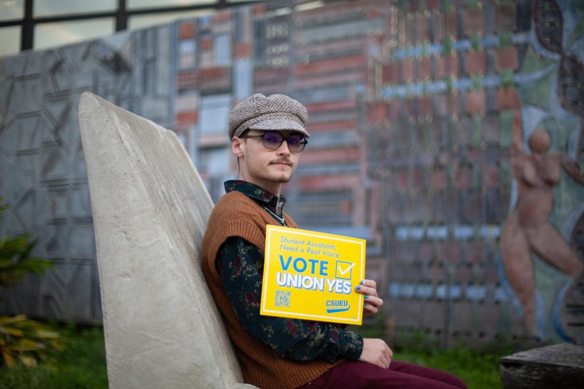 Maddux Eckerling, a CSUEU-SFSU organizer and first-year student, poses with a CSUEU poster near SFSU’s Fine Arts building on Feb. 2, 2024. (Gustavo Hernandez / Golden Gate Xpress)