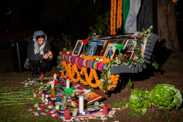 Ziniab Imtair, president of GUPS, crouches to light candles next to a bench in the quad set up as a memorial for a vigil held on the evening of April 29, 2024. (Dan Hernandez / Golden Gate Xpress)