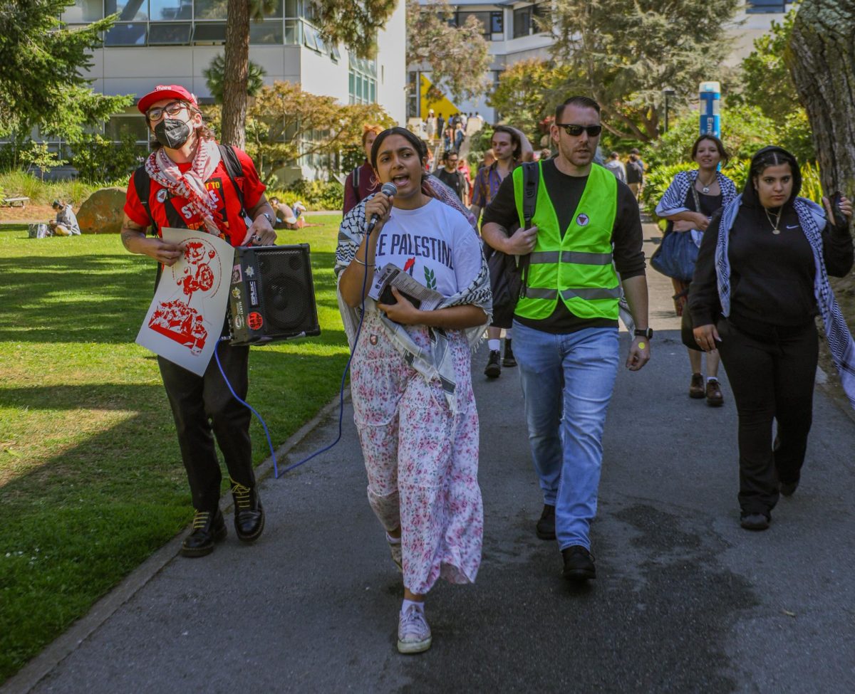 Janet Khanuja lidera a los estudiantes de regreso al edificio de Humanidades después de la demostración de Estudiantes por Gaza en la Plaza Malcolm X. Khanuja corea junto a otros estudiantes mientras caminan el martes 8 de octubre de 2024.  (Gabriel Carver/ Golden Gate Xpress)