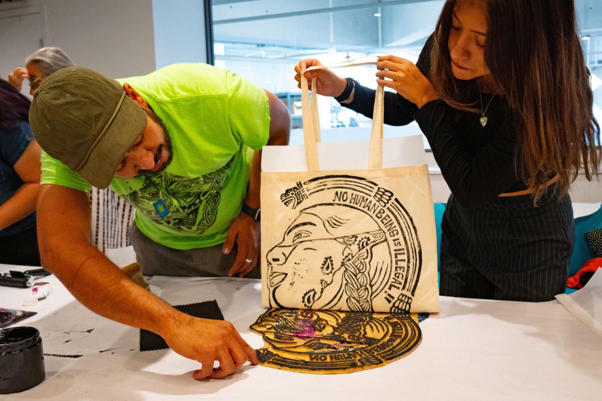 Nicolás González-Medina (izquierda) y Katélyne Gonzalez (derecha) terminan de serigrafiar una bolsa de mano en la sala del Club Universitario ubicado en el Centro Estudiantil César Chávez el miércoles 30 de octubre de 2024. (Jesus Arriaga / Golden Gate Xpress)