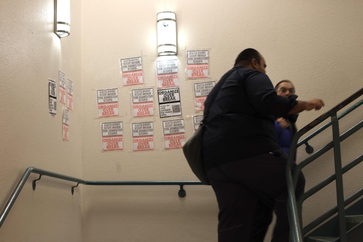 Students walk past flyers on a wall in a Humanities Building stairwell on Tuesday, Dec. 10, 2024. (Gabriel Carver / Golden Gate Xpress)