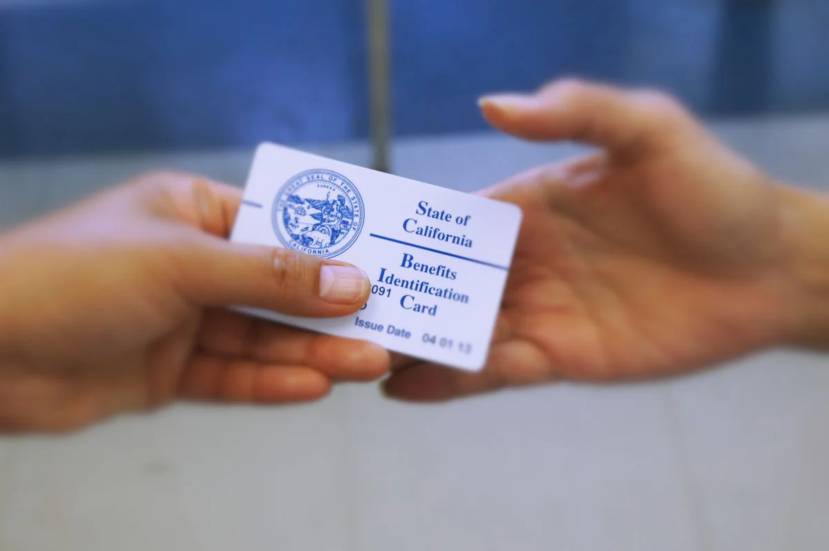 An exchange of a California benefits identification card between two individuals. (Photo courtesy of NLSLA.org)